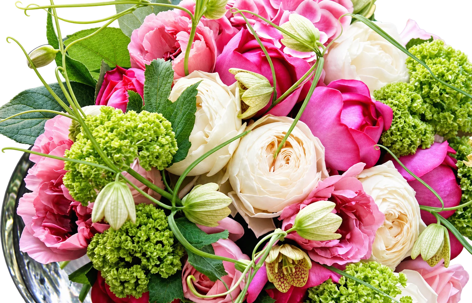 Gros plan sur un bouquet de fleurs composé de pivoines roses, de renoncules blanc crème et de boules de viorne vertes, présenté dans un vase en verre.