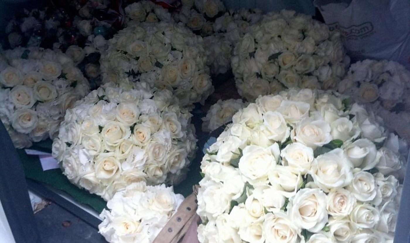 De nombreux bouquets ronds de roses blanches et d'hortensias sont disposés dans le coffre d'un véhicule, prêts à être livrés.