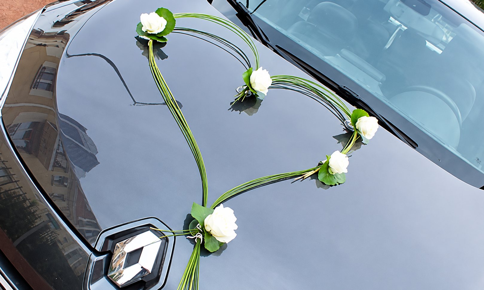 Un cœur formé de tiges vertes et orné de roses blanches décore le capot gris d'une voiture Renault pour un mariage.